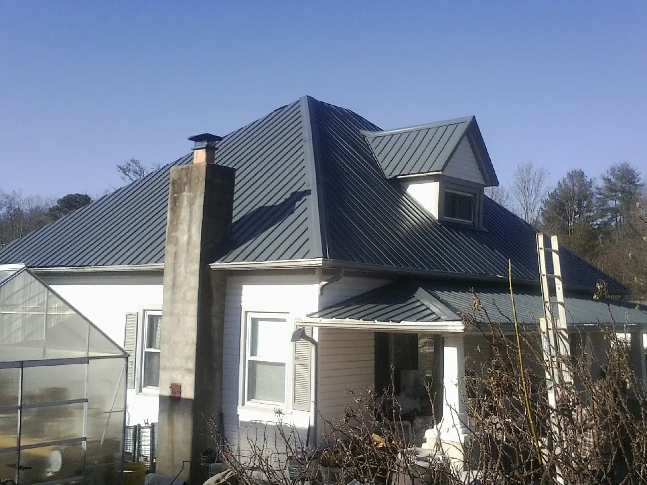 Dark blue standing seam metal roof on a white farmhouse with dormer — Slate & Tile Roof Repair by Roofing Brothers in Roper