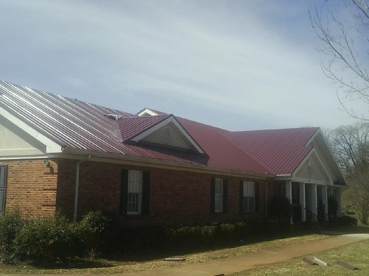 Red metal roof with gabled entries on a long brick building, from a Hail Damage Roof Repair job in Roper