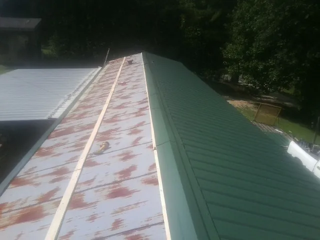 Old rusted panels beside newly installed green metal roofing — Wind Damage Roof Repair by Roofing Brothers in Roper