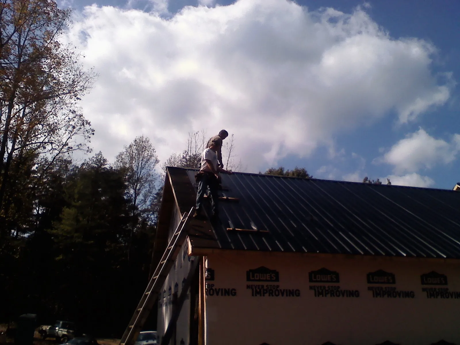 Roofer fastening dark metal panels high against a cloudy sky, from a Roof Inspection job in Roper