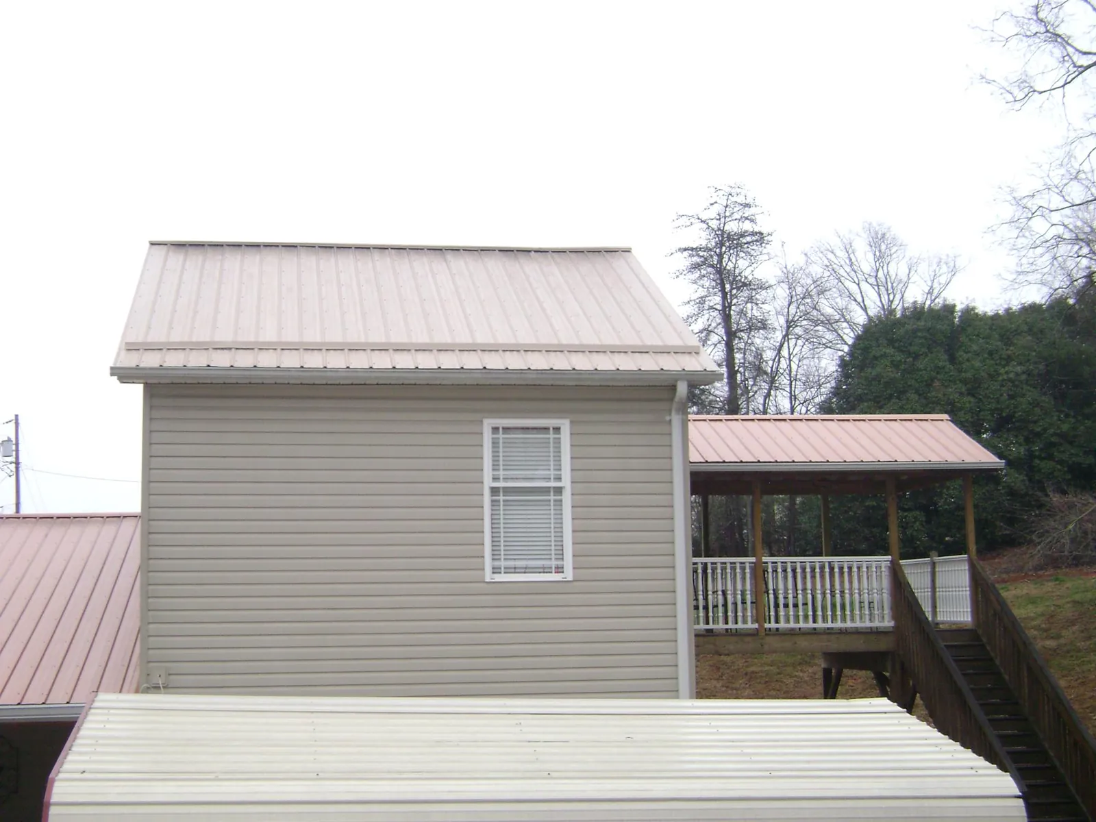 Tan metal roofs on a two story addition and attached porch, from a Roof Replacement job in Roper